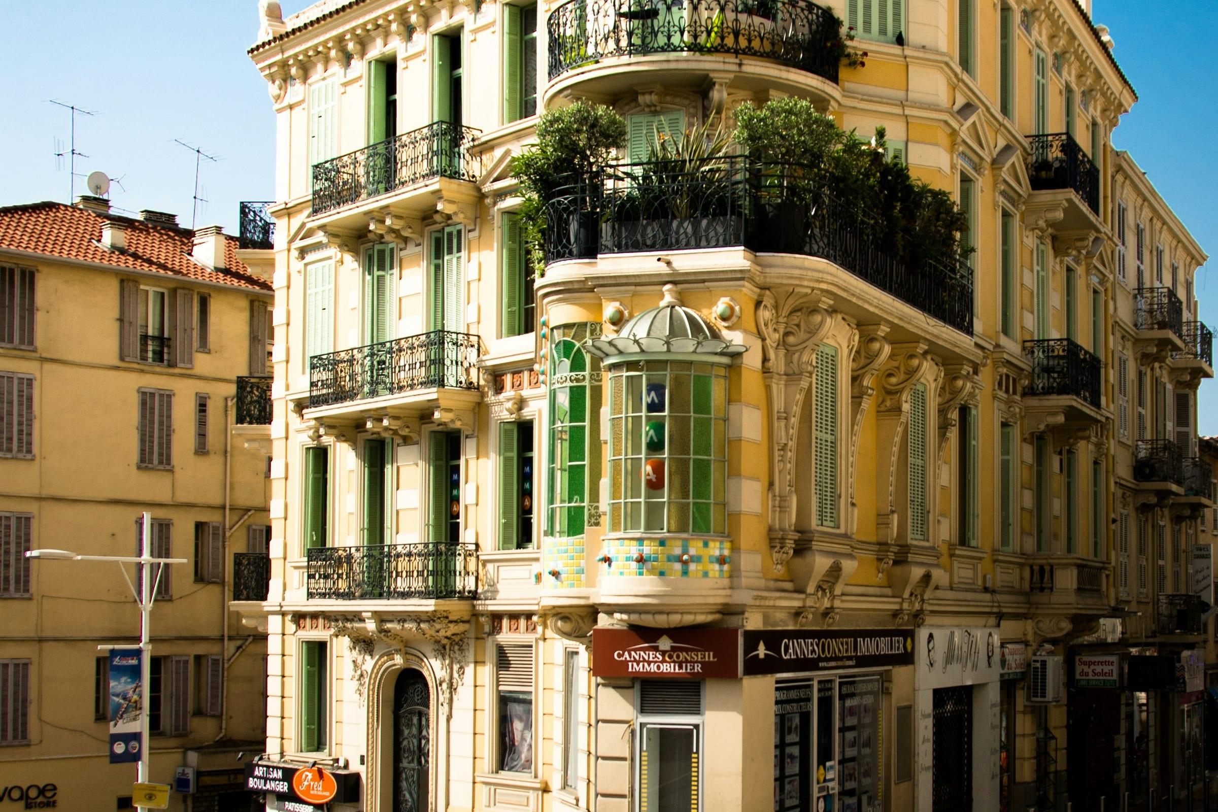 A Belle Époque corner frontage in Cannes, shuttered balconies and bay windows above the street.