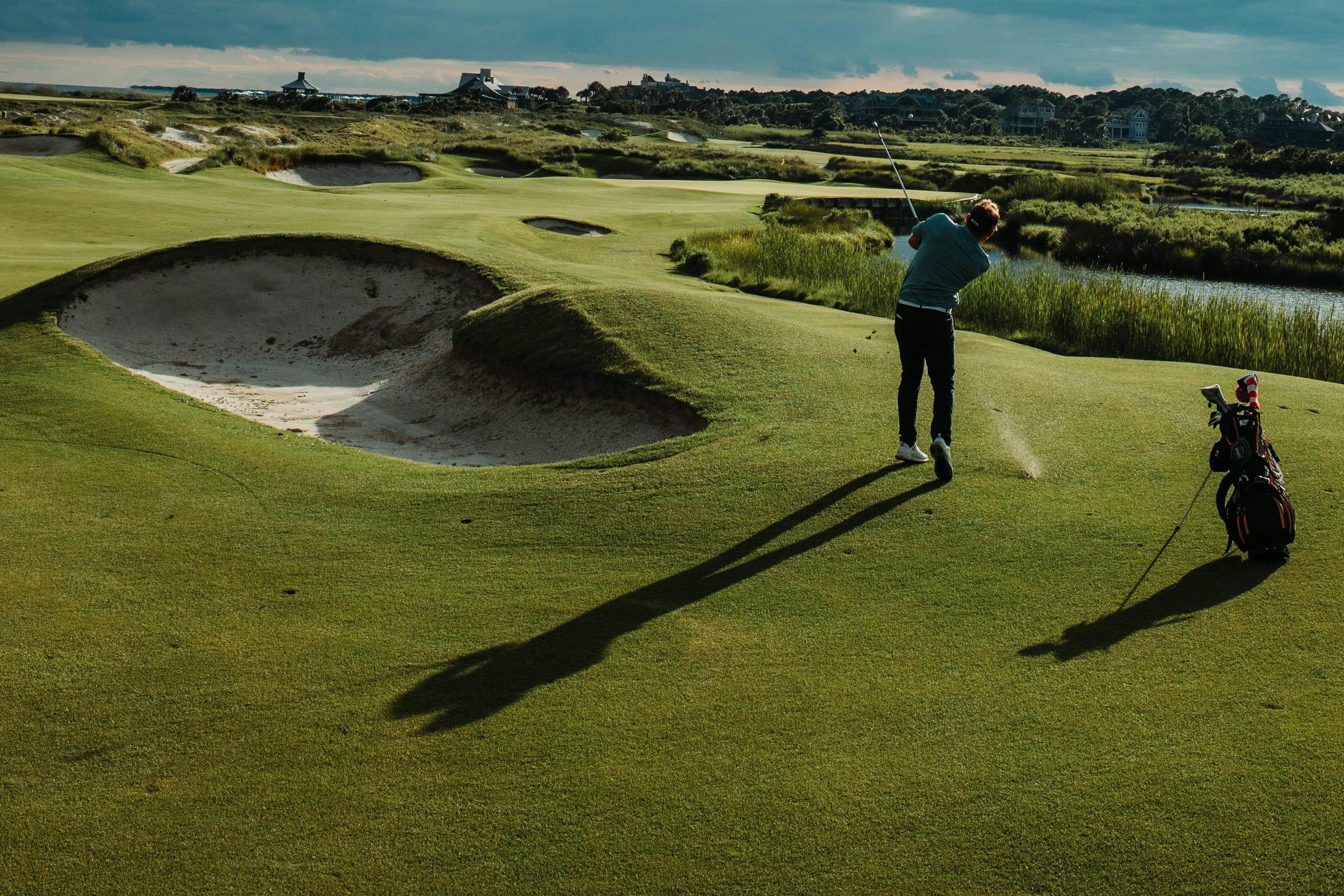 A championship hole in low sunlight, deep bunkers short of the green and a player on the fairway.