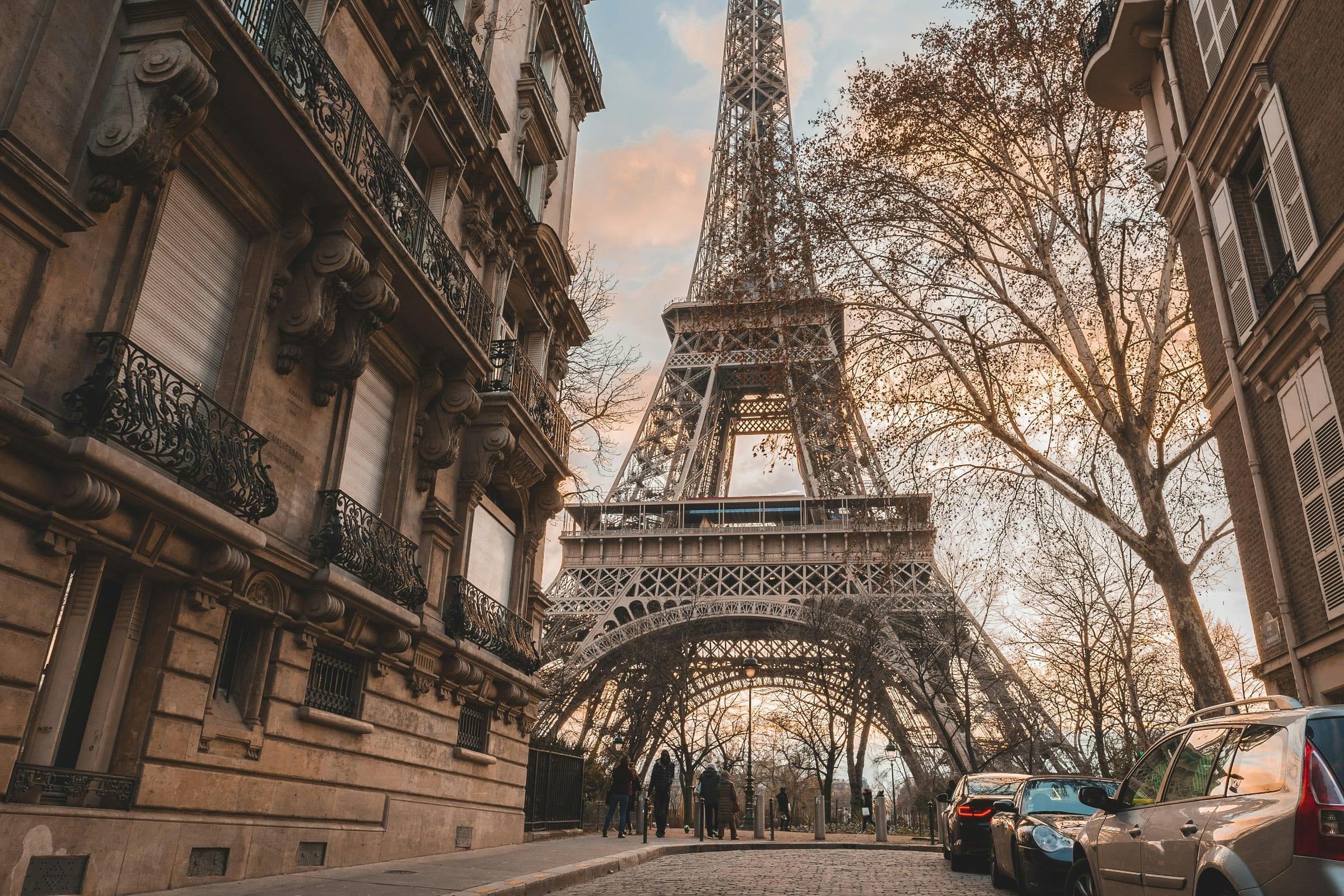 The Eiffel Tower at the end of a Paris street, bare trees and a stone façade in the foreground.