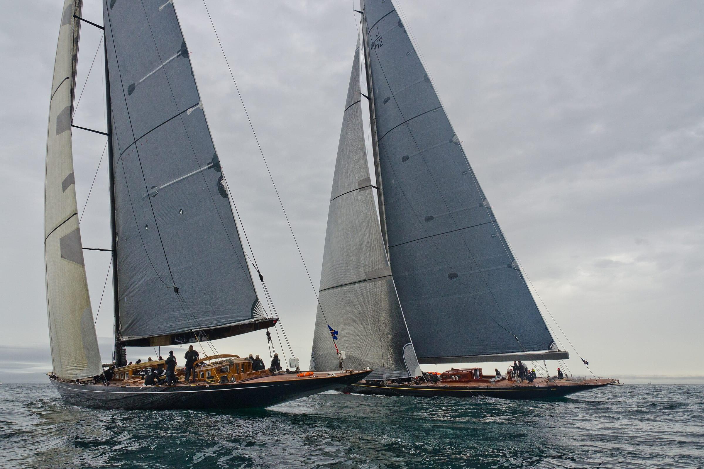 Two classic J-class yachts racing under full sail on open water.