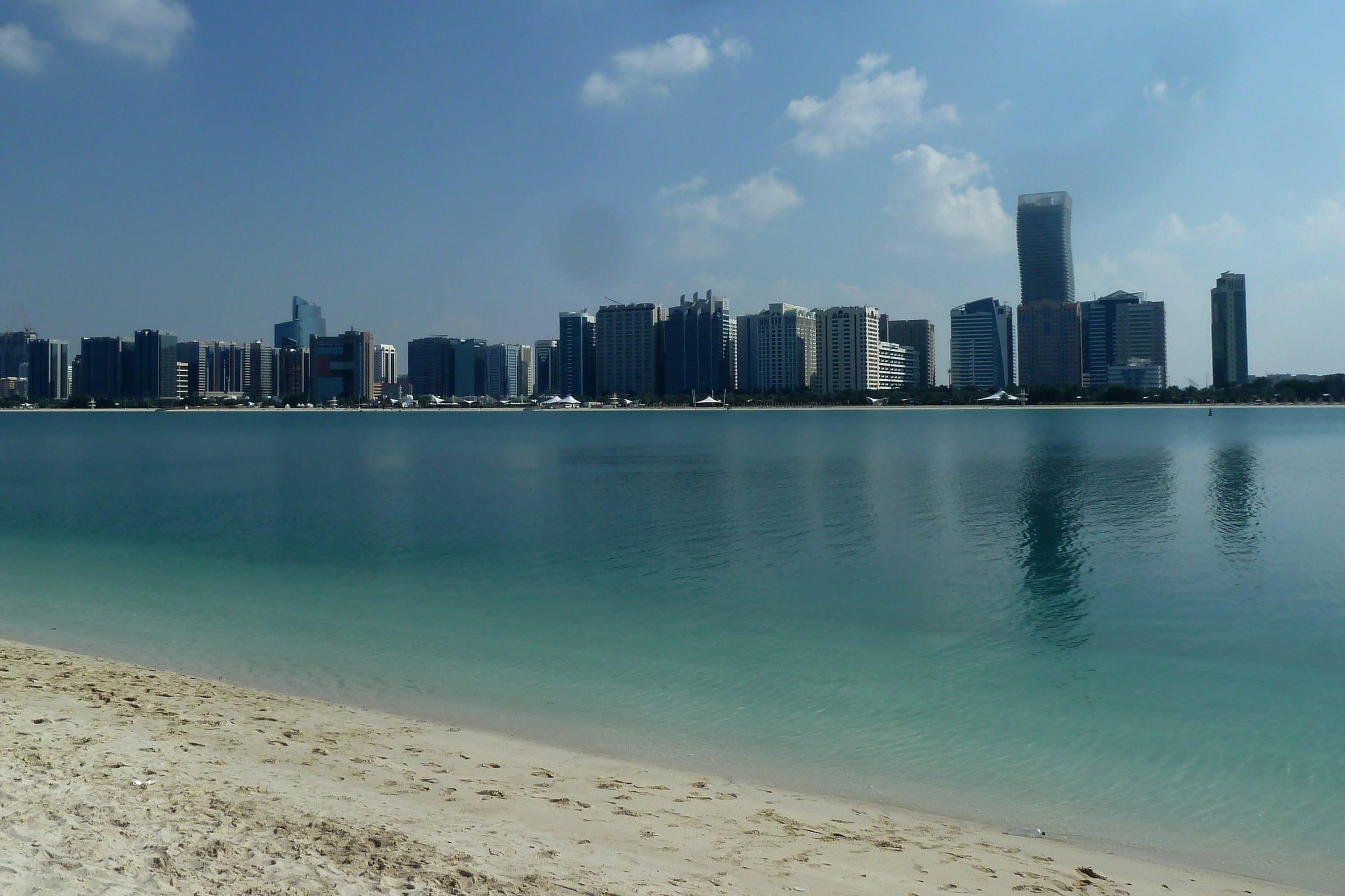 The Abu Dhabi corniche and city skyline seen across shallow turquoise water.