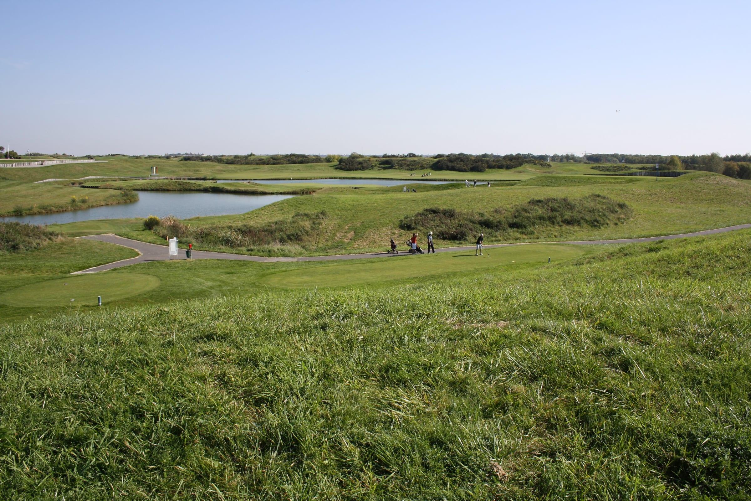 A championship green at Le Golf National beyond an open water hazard, dune mounding around it.